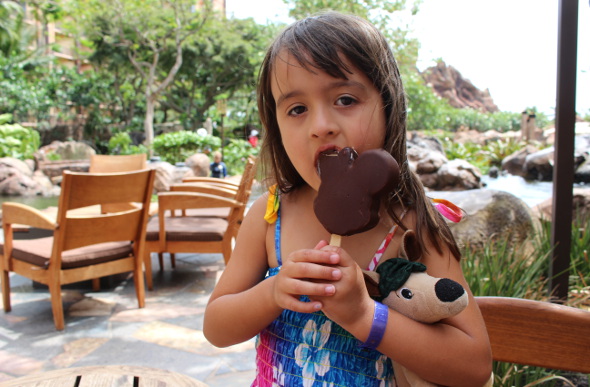 A little girl eats a Mickey Mouse ice-cream outside at the resort