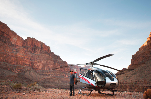 A man stands outside a helicopter that has landed on the floor of the Grand Canyon