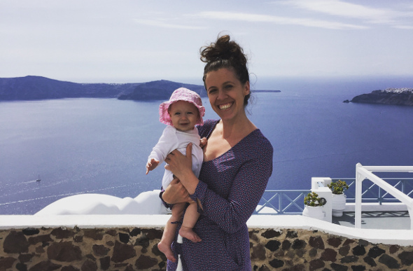 A mother carrying her baby stands in front of the brilliant blue sea in Santorini