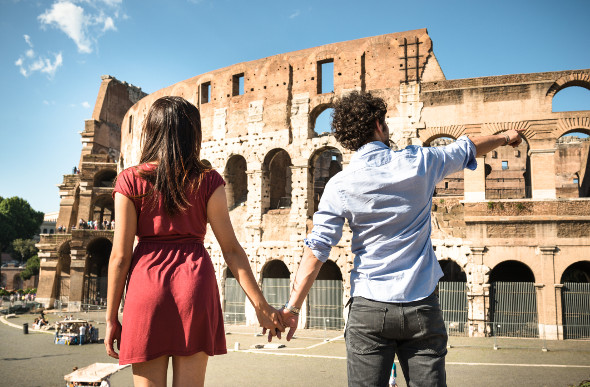 A young couple stands in front looking at the Colosseum in Rome