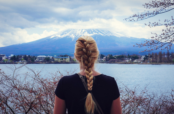 A young blonde women looks at Mount Fuji in the distance with her back to the camera