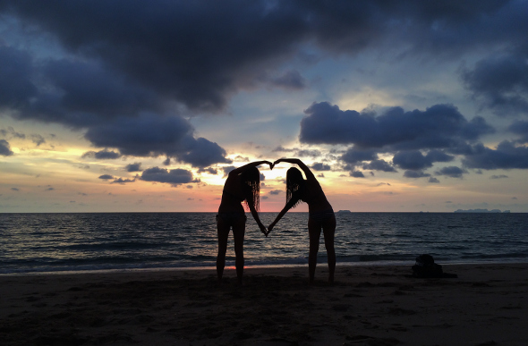 Two females making a heart shape with their arms at sunset on a Thailand beach
