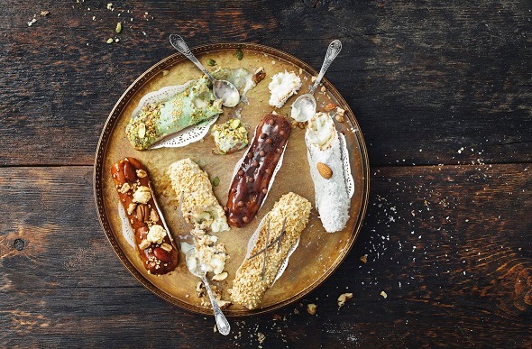  Flat-lay image of chocolate and pistachio eclairs on a gold platter and wooden table.