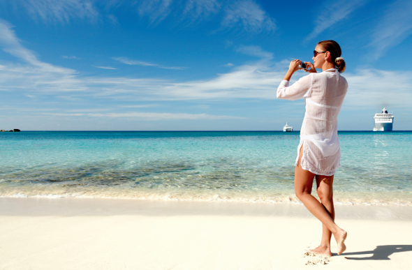 Woman taking a picture on the beach with a cruise ship in the background