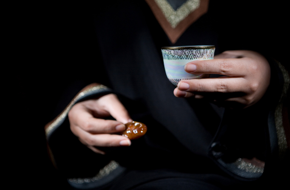An Arabic woman holds a cup of strong coffee, or gahwa, served with dates.