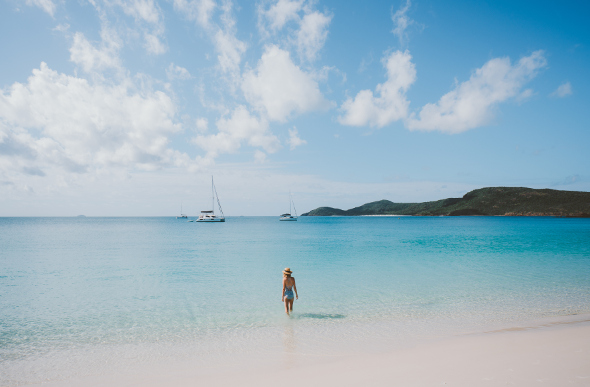 Instagrammer Emilie Ristevski steps into the surreal blue waters of Whitehaven Beach, with moored yachts in the background.