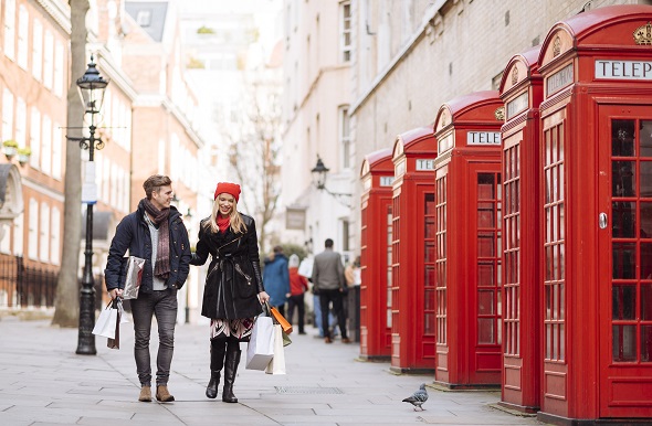  A couple walking down the street in London next to a row of telephone boxes.