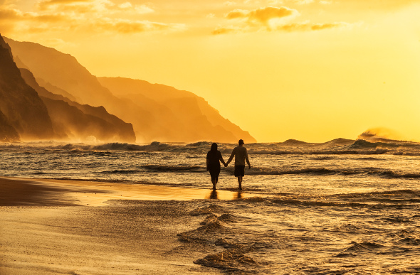 A couple walking along a beach in Hawaii during sunset