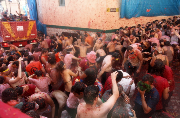 People covered in tomatoes, throwing tomatoes during La Tomatina