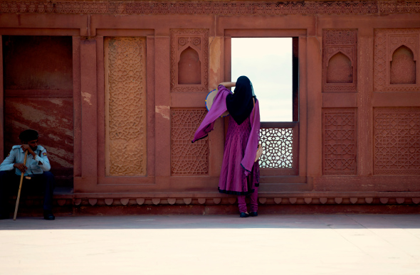 A woman dressed in purple standing beside a burnt-orange wall