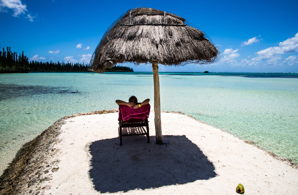 A person sits under a beach umbrella in New Caledonia.