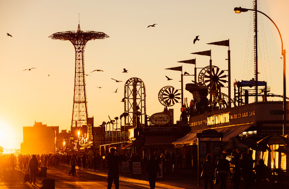 Carnival rides line the boardwalk at Coney Island in New York at sunset.