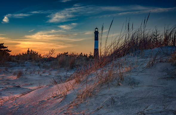The sun sets behind a lighthouse on Fire Island.