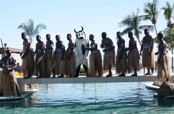The Cash Cow and Fijian warriors cross a narrow bridge over the resort pool.