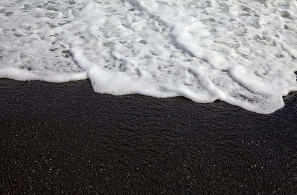 A close-up of black sand meeting white sea foam in Tahiti.