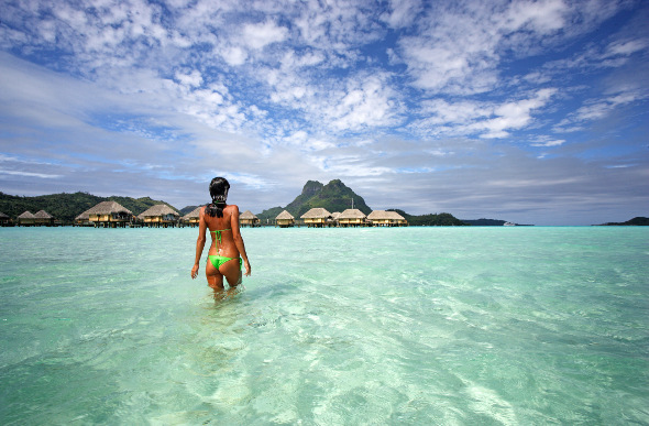 A woman in a bikini wades into the crystal-clear waters of Bora Bora Lagoon in French Polynesia.