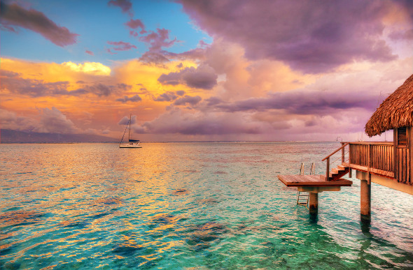 A golden sunset over the waters of Tahiti, with a boat in the background and an underwater bungalow in the foreground.