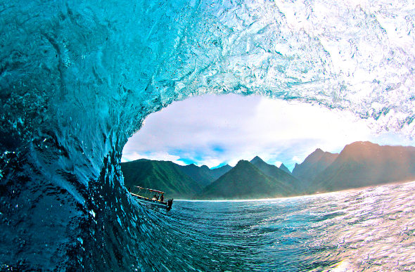 The mountainous shoreline can be seen through a curling wave at Teahupo'o in Tahiti.