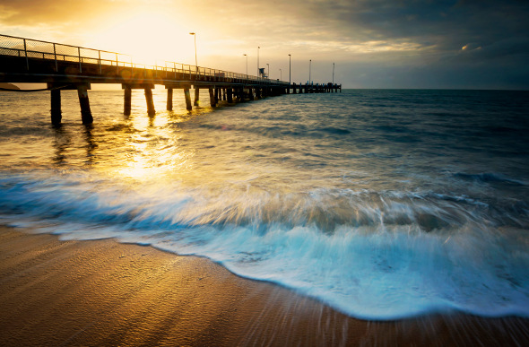 Sunset bathes a pier in Cairns in a golden glow as the foamy tide rolls in.