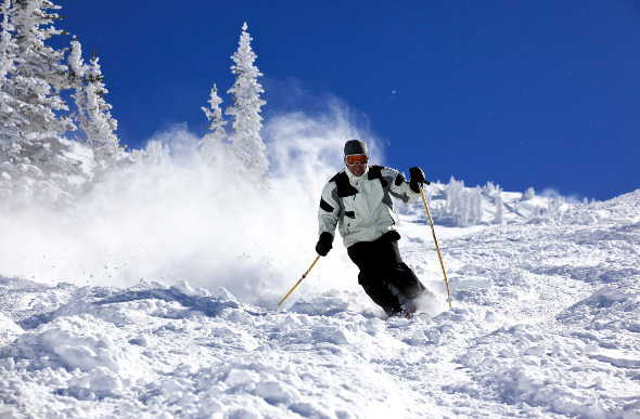 A skier kicks up powder on a blue-sky day at Snowbird ski resort in Utah.
