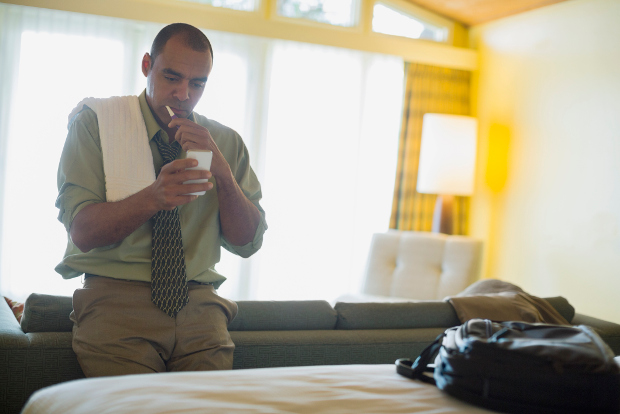 A businessman cleans his teeth in his hotel room.