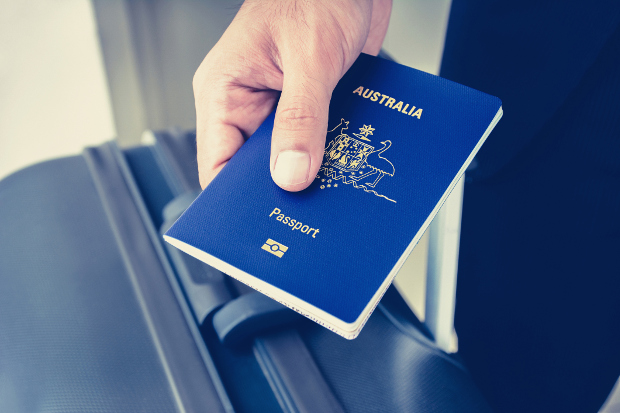 A man holding an Australian passport along with his suitcase