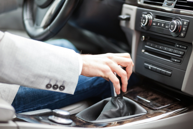 A close up of a hand reaching for the gear shift while driving a car