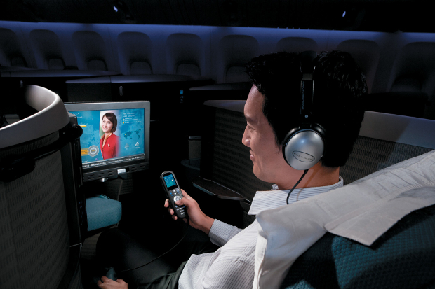 A man with headphones on looking at the Cathay Pacific entertainment system