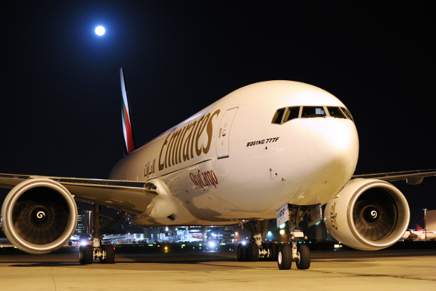 An exterior view of an Emirates 777 aircraft sitting on the runway at night