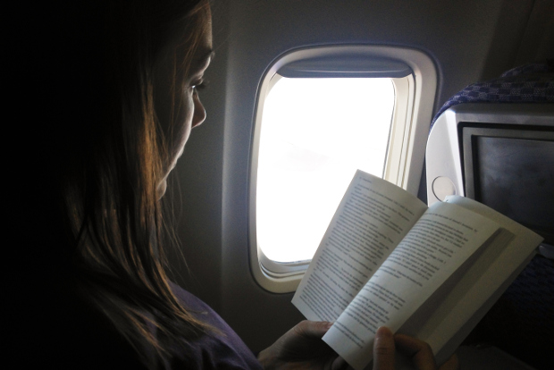 A woman reads a book while travelling on a plane.
