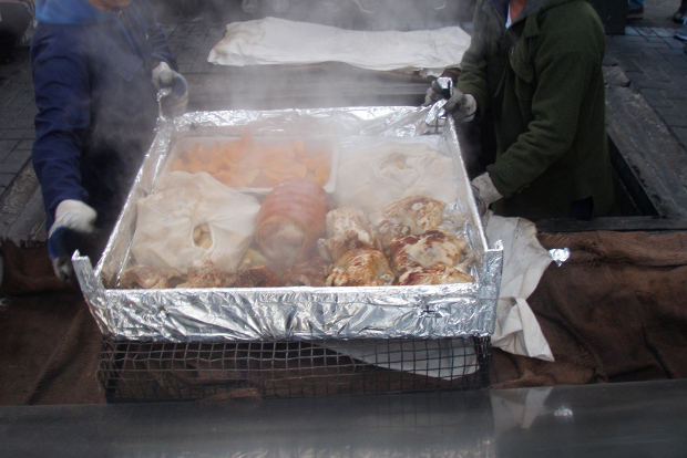 Two men pulling a large tray of food out of a hangi oven