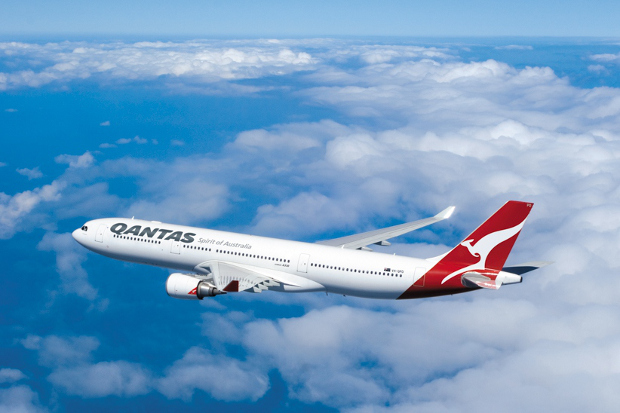 Qantas plane flying through a blue sky with scattered clouds