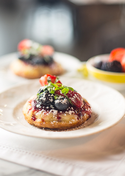 A crumpet on a plate topped with berries and syrup