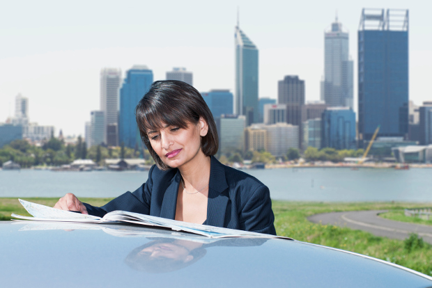 A woman reads a map on the roof of her car, with a city skyline behind her.