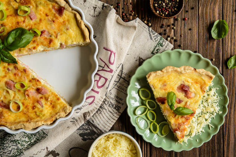 quiche lorraine in pan from above with slice on separate plate.