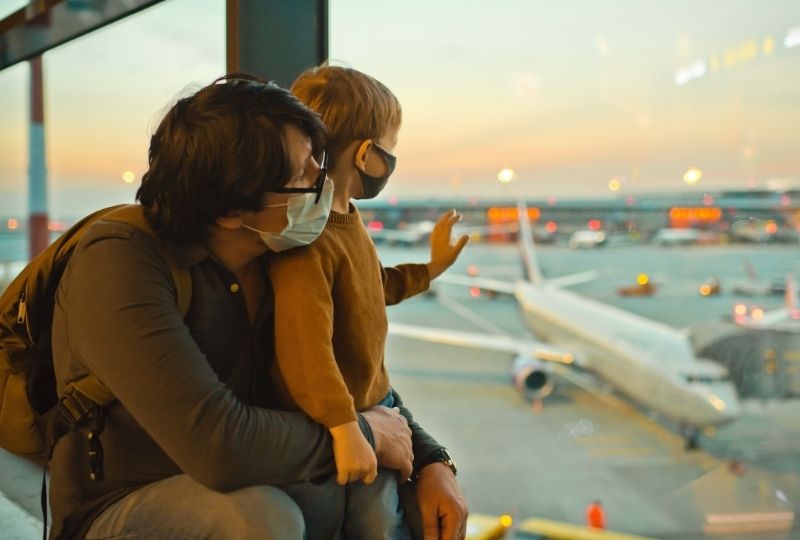 Father and child wearing masks looking out an airport window.