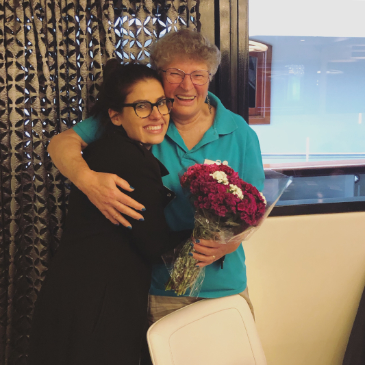 Sheridan and Aida hugging and smiling towards the camera. Aida holding a punch of flowers