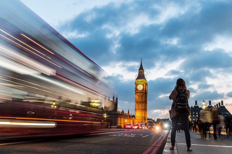 A woman takes a photo of Big Ben as a bus whizzes by in London's twilight.