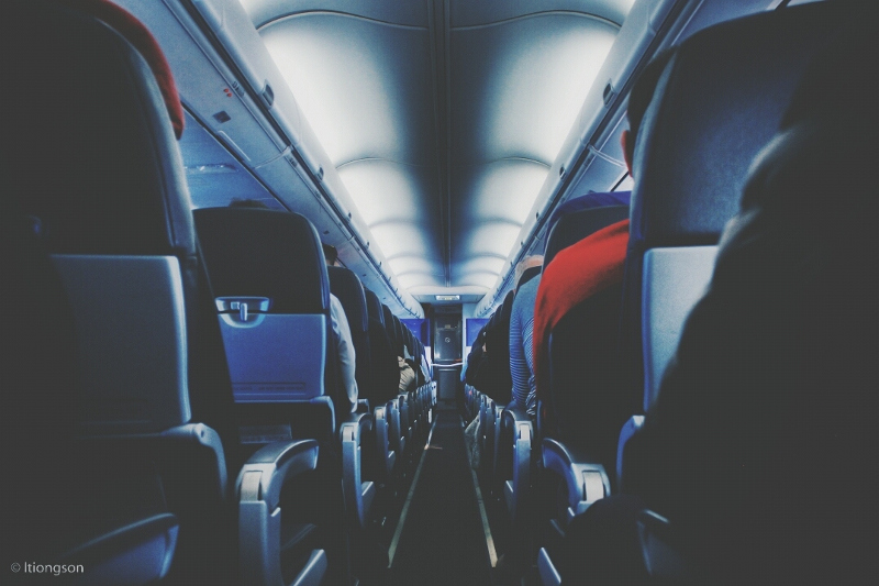 A view down the aisle of an aircraft, showing passengers in their seats from behind.