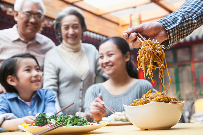 A man serves noodles at an Asian family's table.