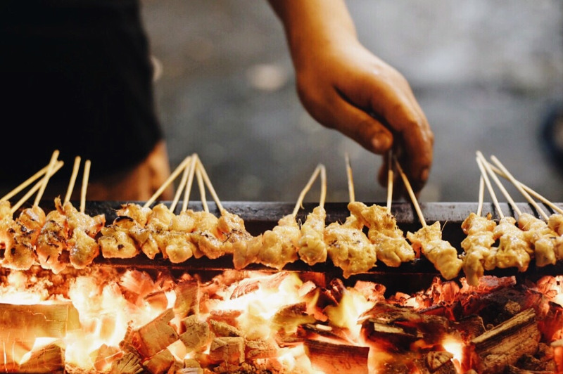 A close-up of a hand cooking satays over a fire in Kuala Lumpur, Malaysia.