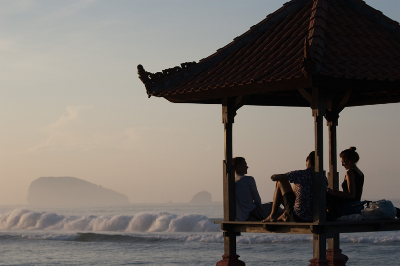 Young people relax in a Balinese pagoda as the waves roll in to Candidasa, Bali.