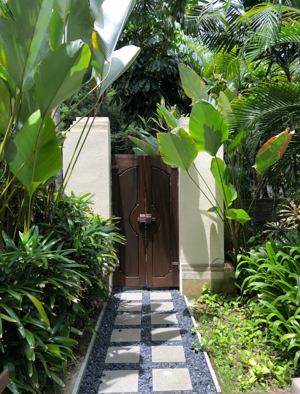Lush tropical garden with stone pathway leading to a wooden door.
