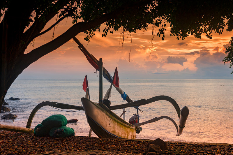 A jukung fishing boat forms an unusual silhouette against the setting sun at Amed Beach in Bali.