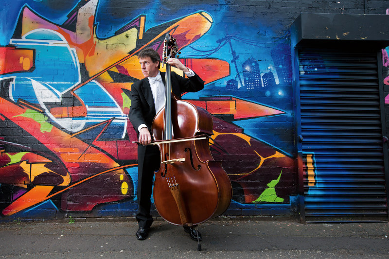 A man plays the cello near a graffiti-covered wall in Birmingham, UK.