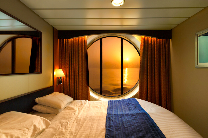 A cruise ship cabin with a porthole looking out to sea.