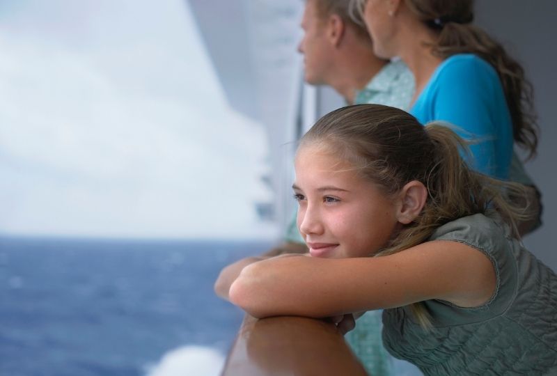 Girl leaning over a railing on a cruise ship with parents in the background