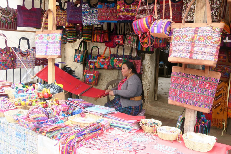 A woman sells colourful handcrafted bags and textiles in a market stall in Guatemala.