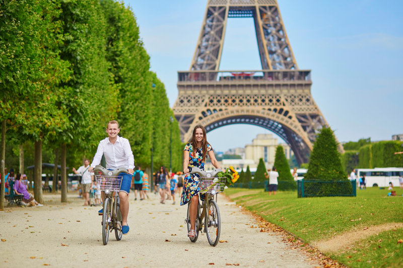 A couple ride bikes past the Eiffel Tower in Paris, France.
