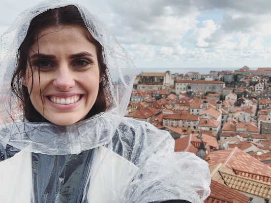 Sheridan taking a selfie wearing a poncho, with old town of dubrovnik in the background